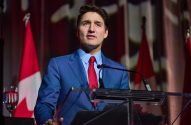 O primeiro-ministro Justin Trudeau discursa em um pódio com bandeiras do Canadá ao fundo.