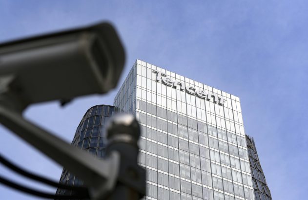 Prédio da Tencent com câmera de segurança desfocada em primeiro plano contra céu azul.