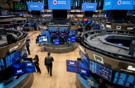 O pregão da Bolsa de Nova York (NYSE) com mesas circulares, telas exibindo ações e logos da Cruz Vermelha.