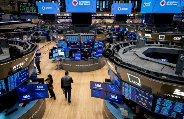 O pregão da Bolsa de Nova York (NYSE) com mesas circulares, telas exibindo ações e logos da Cruz Vermelha.