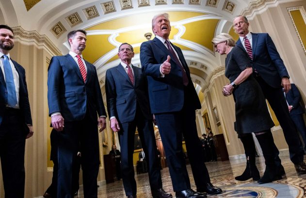 Donald Trump gesticulando e falando em corredor formal, acompanhado por pessoas em terno.