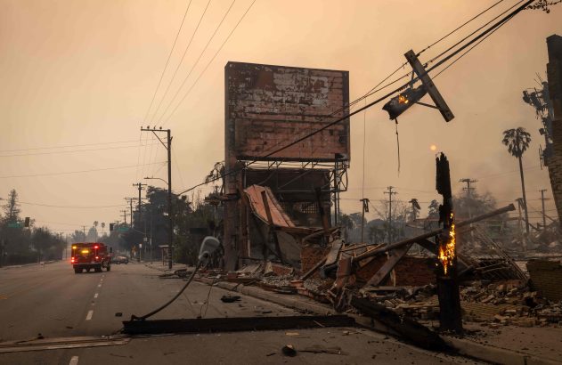 Destruição por incêndio: edifícios e postes em chamas, escombros em rua. Caminhão de bombeiros. Céu alaranjado.