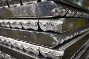 Pilha de lingotes de metal prateado com arestas onduladas, empilhados.