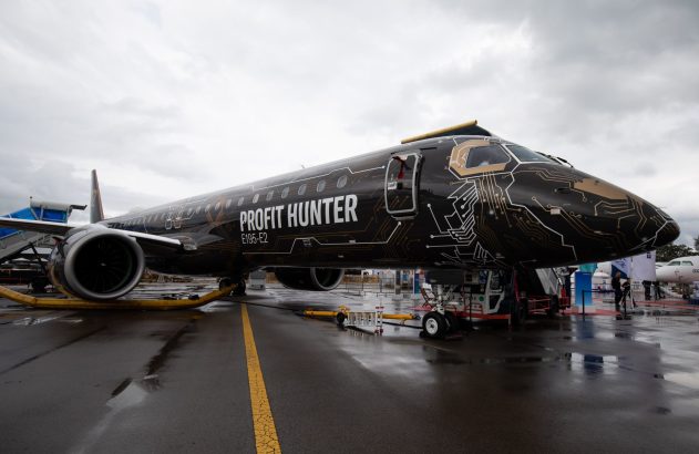 Jato preto "Profit Hunter" E195-E2 com estampa de circuito, parado em pátio molhado. Céu nublado.