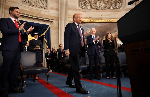 Donald Trump caminha à frente; J.D. Vance, Joe Biden e Kamala Harris aplaudem em salão.