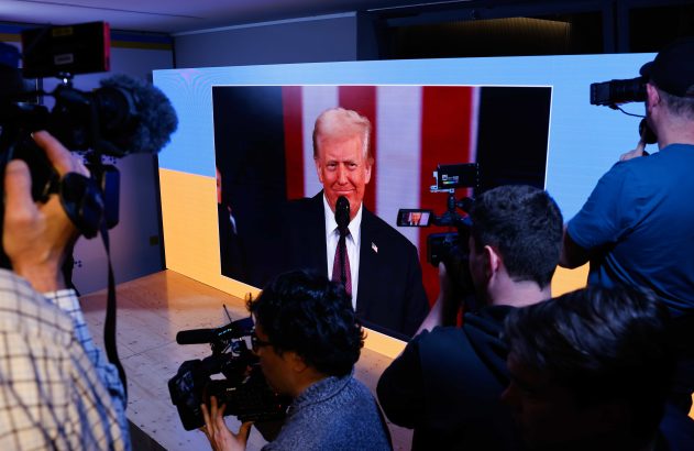 Cinegrafistas filmam Donald Trump em telão durante evento.