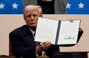 Donald Trump mostra memorando assinado sobre congelamento de contratações federais, com estrelas ao fundo.