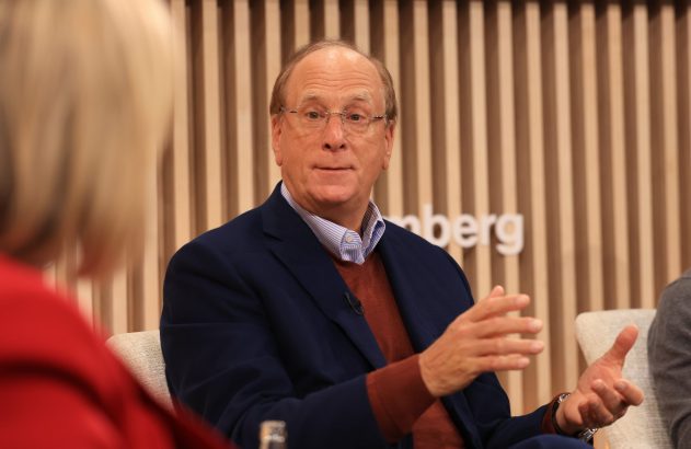 Homem de óculos, blazer azul e suéter marrom, fala e gesticula. Fundo desfocado com logo da Bloomberg.