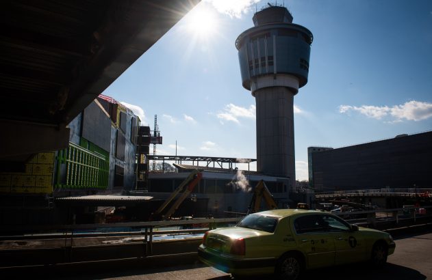 Táxi amarelo, torre de controle de aeroporto e canteiro de obras sob sol forte.