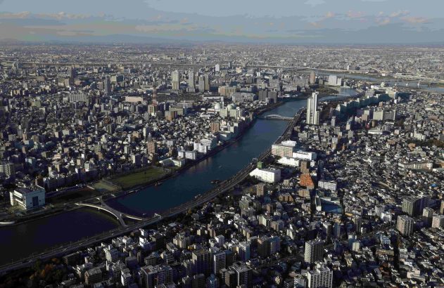 Vista aérea de uma vasta metrópole com rio sinuoso, muitos edifícios e várias pontes, sob céu parcialmente nublado.