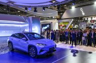 BYD Sealion 7 roxo em estande de feira, iluminado em azul. Pessoas observam o carro em exibição.