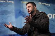Volodymyr Zelenskyy, de barba e jaqueta escura, gesticula com as mãos abertas enquanto fala em evento da Bloomberg.