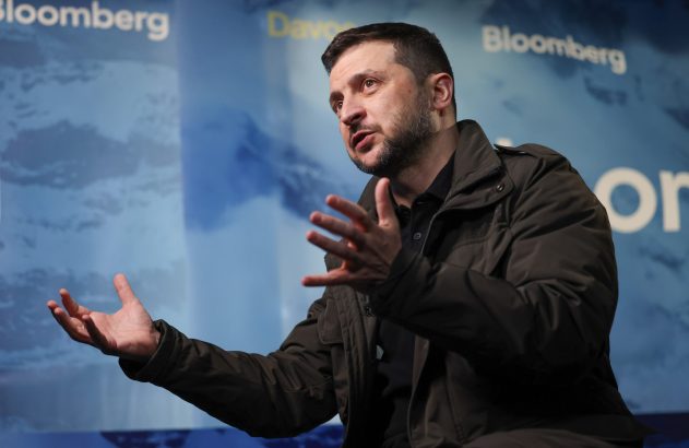 Volodymyr Zelenskyy, de barba e jaqueta escura, gesticula com as mãos abertas enquanto fala em evento da Bloomberg.