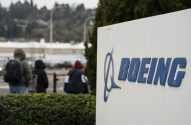 Letreiro da Boeing em primeiro plano; pessoas caminham ao fundo sob céu nublado.