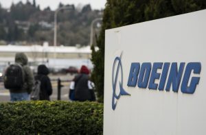 Letreiro da Boeing em primeiro plano; pessoas caminham ao fundo sob céu nublado.
