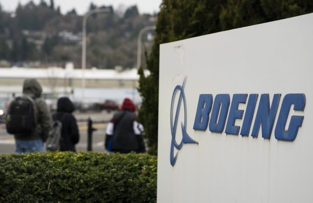 Letreiro da Boeing em primeiro plano; pessoas caminham ao fundo sob céu nublado.