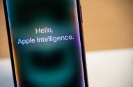 Celular com texto 'Hello, Apple Intelligence' na tela, sobre fundo turvo.