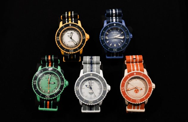 Cinco relógios Scuba Fifty Fathoms coloridos (amarelo, azul, verde, cinza, laranja), da Blancpain X Swatch, em fundo preto.