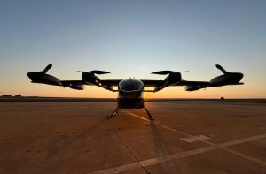 eVTOL (táxi aéreo) em silhueta na pista ao pôr do sol. Sol brilha atrás da aeronave.