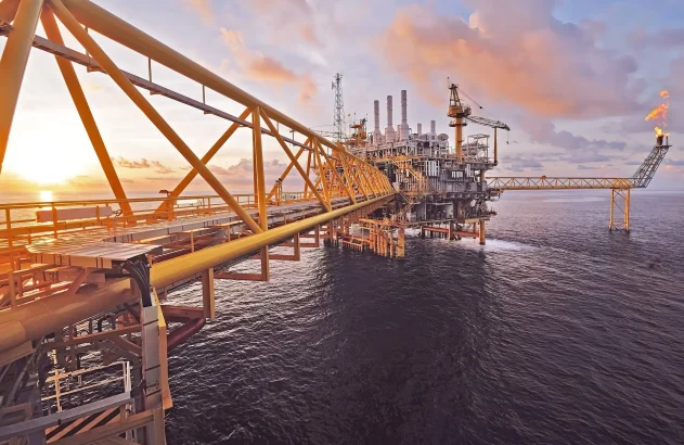 Plataforma de petróleo industrial no oceano ao pôr do sol, com um flare de gás aceso.