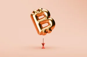Balão dourado em forma de "B" flutua sobre fundo pêssego, equilibrado delicadamente em uma ponta de um pin vermelho.