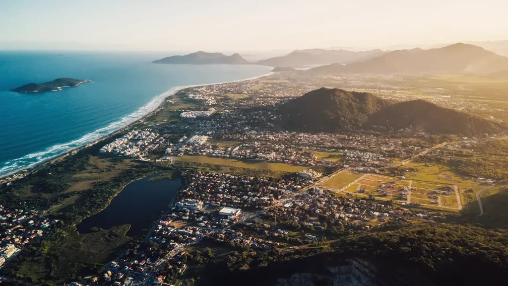 Panorama costeiro com áreas verdes, colinas e montanhas distantes.