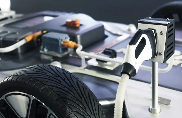 Imagem de um carregador moderno para veículos elétricos, com conector preto e branco, pneu detalhado, e seção de bateria com cabos pretos, brancos e laranjas em um ambiente iluminado.
