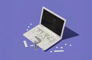 Um laptop branco danificado com teclado quebrado e tela rachada, possivelmente indicando reparo ou dano intencional.