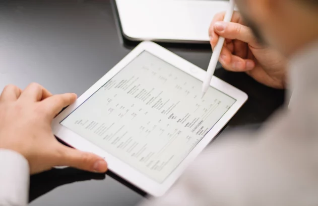 Mãos usando stylus em tablet branco com documento. Laptop no fundo.