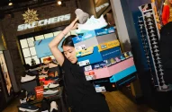 Mulher equilibra caixas de sapatos em loja Skechers com tema natalino.