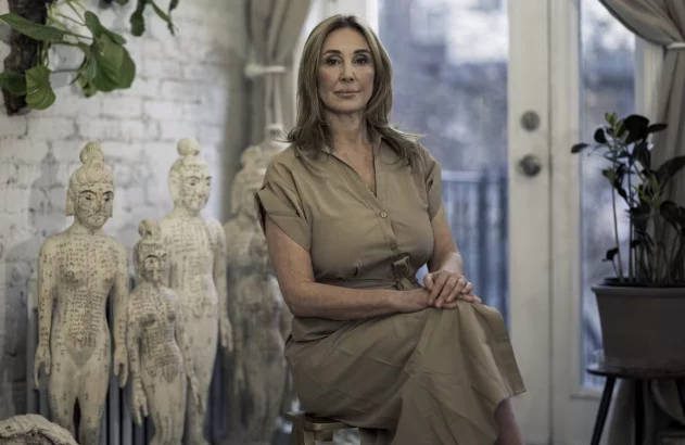 Mulher sentada, olhando para câmera, com modelos de acupuntura e plantas.