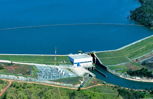 Vista aérea: Barragem hidrelétrica com lago azul, usina e subestação gerando energia.