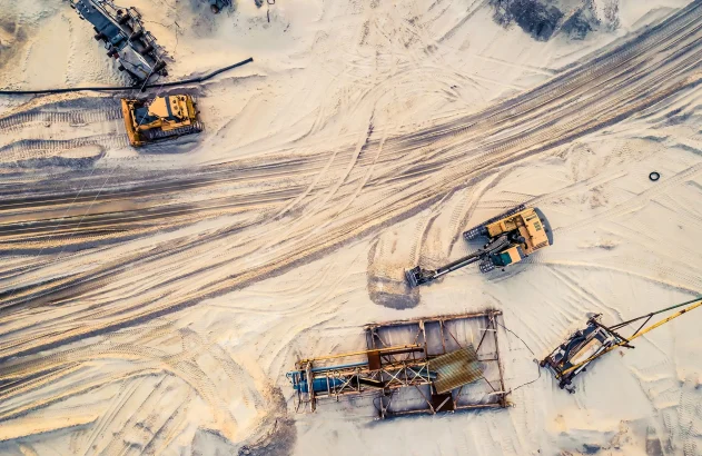 Vista aérea de maquinário pesado em operação de mineração de areia: escavadeira, trator, equipamentos diversos.