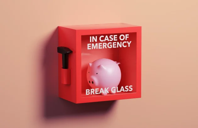 Caixa de emergência vermelha com um cofrinho rosa e a frase "IN CASE OF EMERGENCY BREAK GLASS", acompanhada de um martelo ao lado esquerdo, sobre uma parede pêssego.
