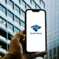 Mão segura smartphone com app da Receita Federal, em frente a um prédio moderno.