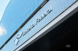Fachada de um edifício moderno da Receita Federal com painéis de vidro refletindo o céu. declaração do MEI