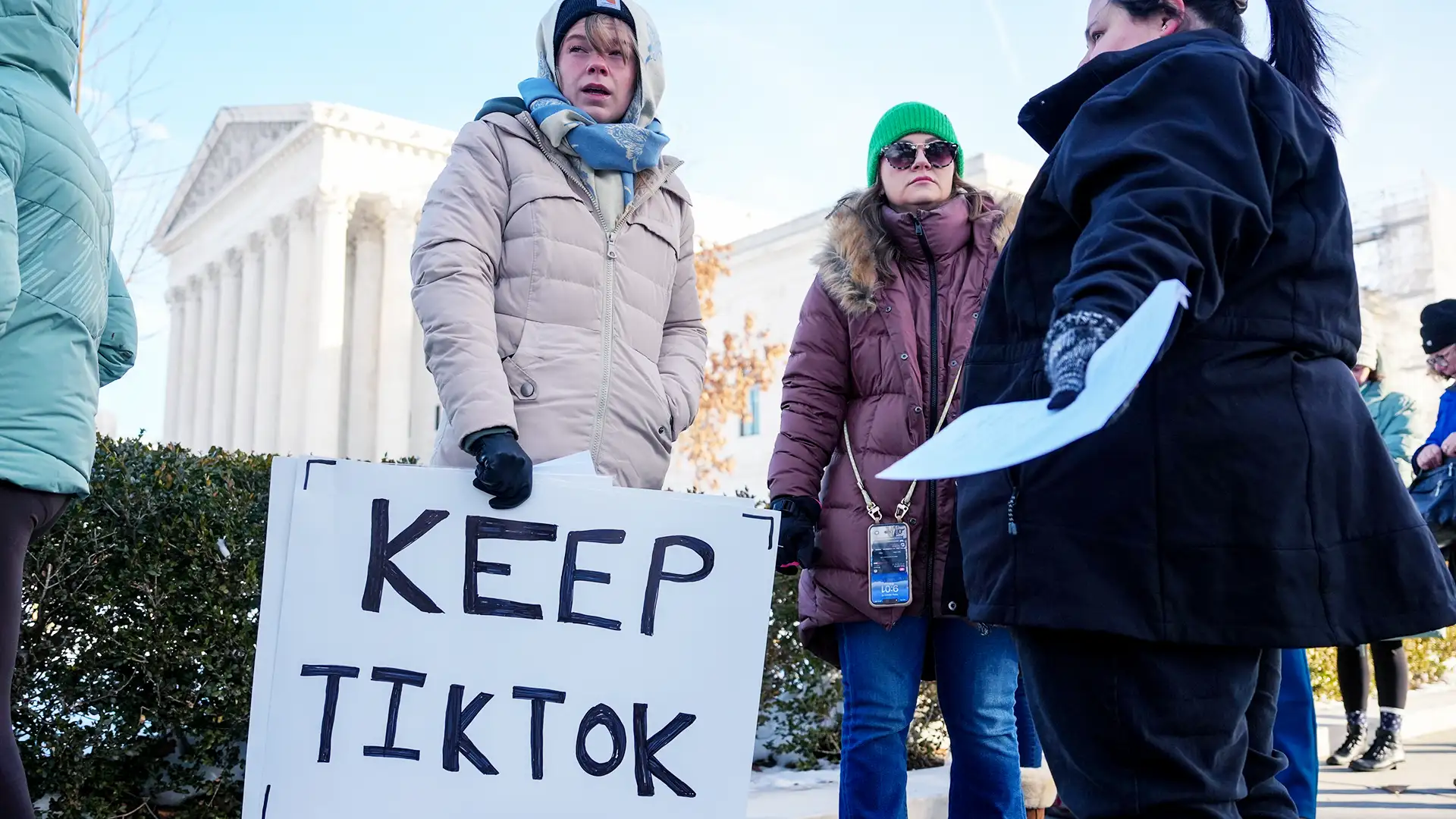 Um grupo de pessoas vestidas para o frio segura um cartaz "KEEP TIKTOK" em frente ao edifício da Suprema Corte dos EUA, sugerindo um protesto relacionado ao aplicativo TikTok.