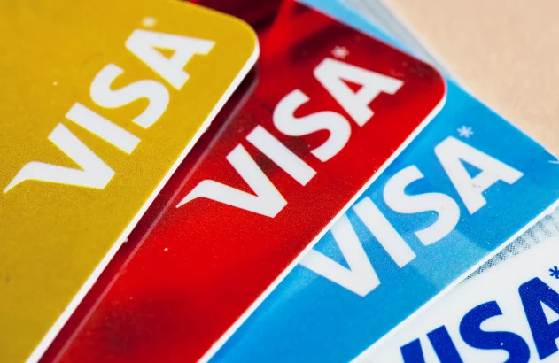 Conjunto sobreposto de quatro cartões Visa em dourado, vermelho, azul e branco, formando um padrão colorido e vibrante.