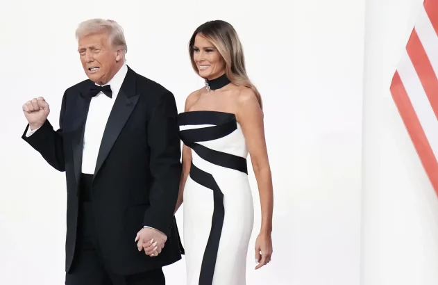 Imagem do presidente dos EUA, Donald Trump, vestindo smoking preto, e da primeira-dama Melania Trump, em vestido branco geométrico, de mãos dadas, com uma bandeira dos Estados Unidos ao fundo.