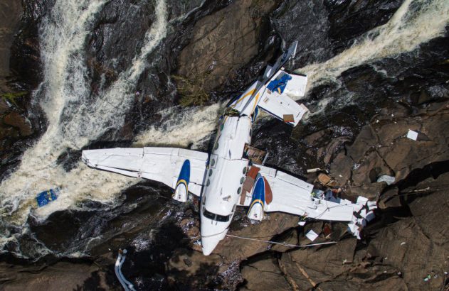Vista aérea de destroços de avião branco em rio com águas turbulentas.