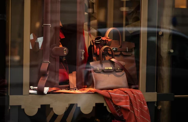 Bolsa marrom e cachecol avermelhado em vitrine de loja. Há reflexos da rua no vidro.