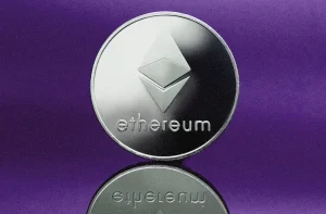 Imagem simbolizando o ethereum, como uma moeda prateada com logotipo tridimensional característico, sobre uma superfície refletiva, destacada por um fundo roxo.
