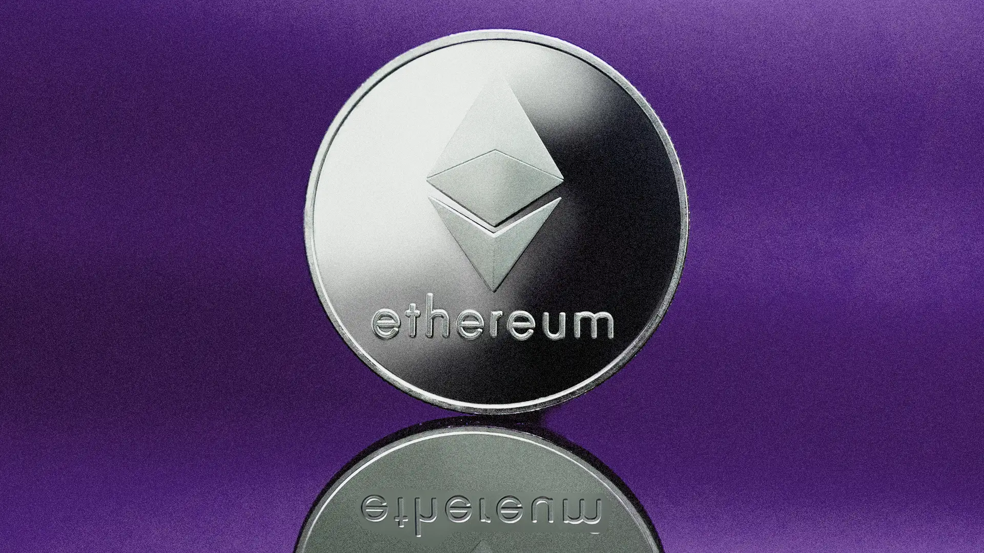 Imagem de uma moeda prateada de Ethereum com seu logotipo tridimensional característico, sobre uma superfície refletiva, destacada por um fundo roxo.