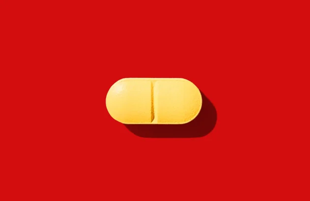 Imagem de um comprimido amarelo oblongo com linha de divisão sobre um fundo vermelho vibrante, com sombra projetada para a parte inferior direita.