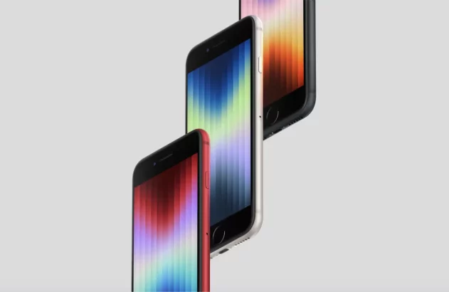 Três smartphones dispostos em diagonal, com telas em gradiente de cores do azul ao vermelho e carcaças nas cores vermelha, prateada e preta, contra um fundo cinza claro.