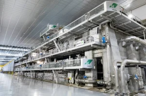 Complexa máquina de produção Klabin/Valmet domina o interior de uma fábrica industrial espaçosa e moderna.