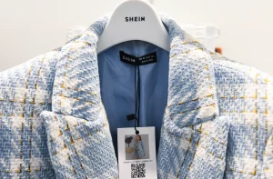 Peça de roupa com padrão xadrez azul claro, cabide branco da marca SHEIN e etiqueta preta indicando tamanho XS.