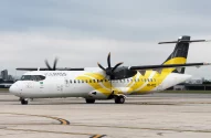 A imagem mostra um avião turboélice ATR da companhia aérea VOEPASS estacionado em um aeroporto urbano, com detalhes em amarelo e cinza sob um céu nublado.