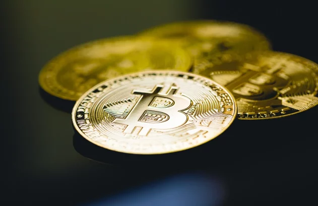 Moedas douradas de Bitcoin sobre fundo escuro, com uma em primeiro plano e nítida.