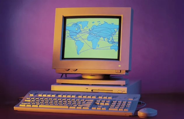 Imagem de um computador retro, com monitor CRT exibindo um mapa-múndi interconectado, em fundo roxo nostálgico.